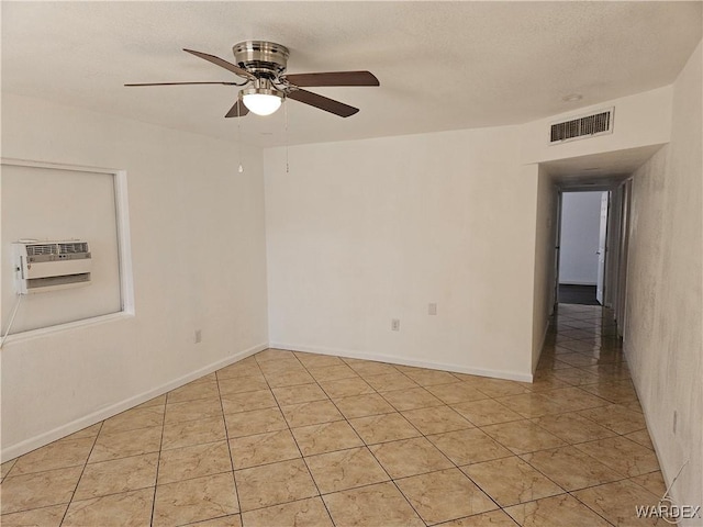 empty room featuring visible vents, a ceiling fan, an AC wall unit, light tile patterned flooring, and a textured ceiling