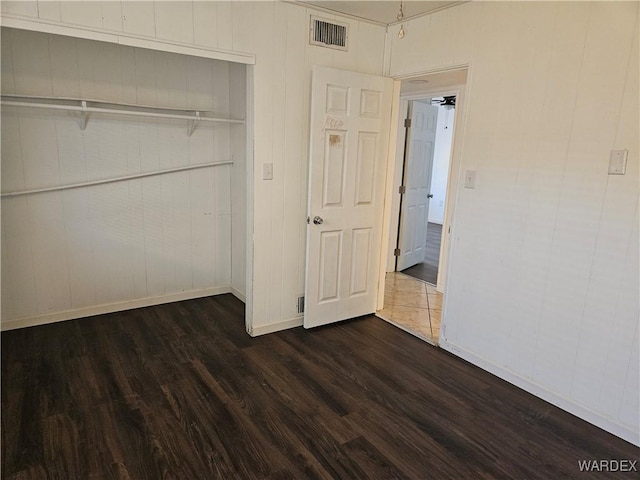 unfurnished bedroom featuring a closet, visible vents, dark wood finished floors, and baseboards