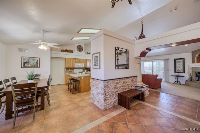 dining room featuring arched walkways, visible vents, a ceiling fan, a tile fireplace, and high vaulted ceiling