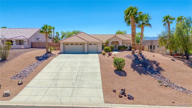view of front facade with a tiled roof, concrete driveway, fence, a garage, and stucco siding