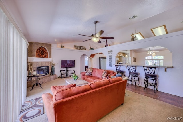 tiled living room with arched walkways, vaulted ceiling, visible vents, a ceiling fan, and a tile fireplace