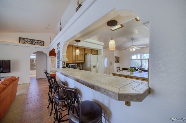 kitchen with vaulted ceiling, white fridge with ice dispenser, a breakfast bar area, arched walkways, and a peninsula