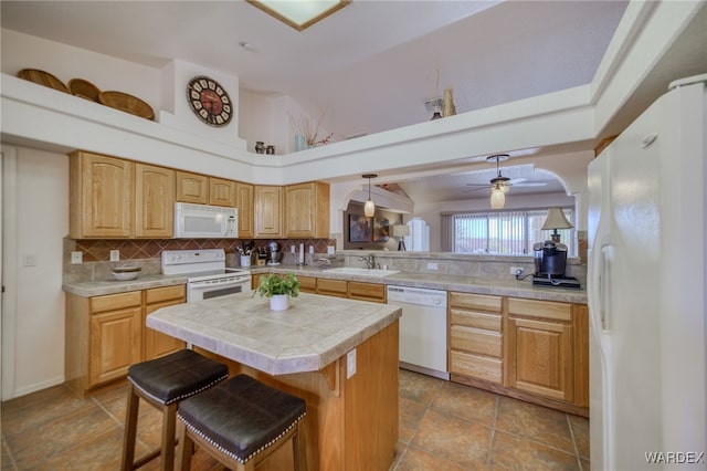 kitchen with a sink, a kitchen bar, decorative backsplash, a ceiling fan, and white appliances