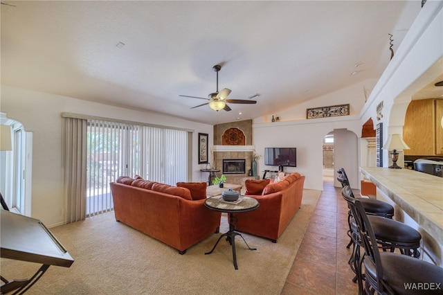 living area featuring lofted ceiling, a fireplace, arched walkways, and ceiling fan