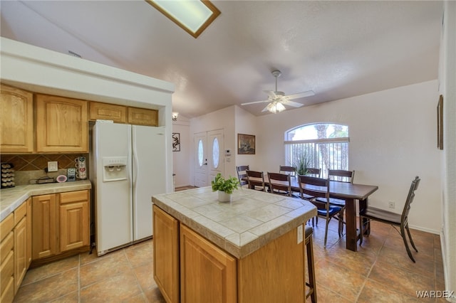 kitchen featuring backsplash, tile countertops, a center island, white fridge with ice dispenser, and ceiling fan
