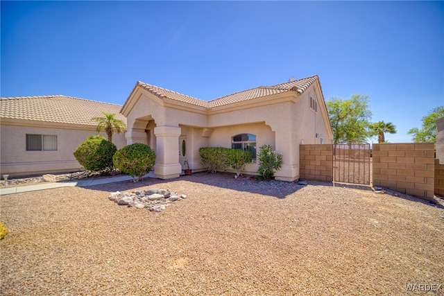 mediterranean / spanish house featuring fence, a tile roof, a gate, and stucco siding