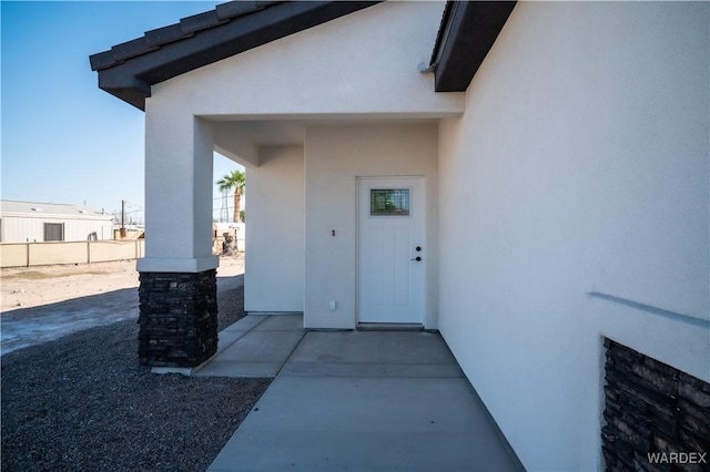 view of exterior entry with fence and stucco siding