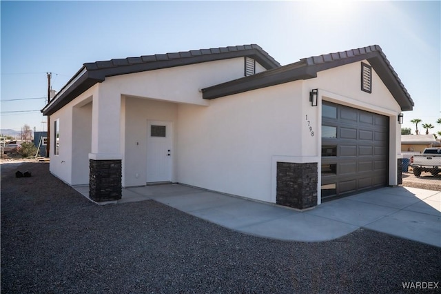 view of side of property featuring stone siding, concrete driveway, an attached garage, and stucco siding