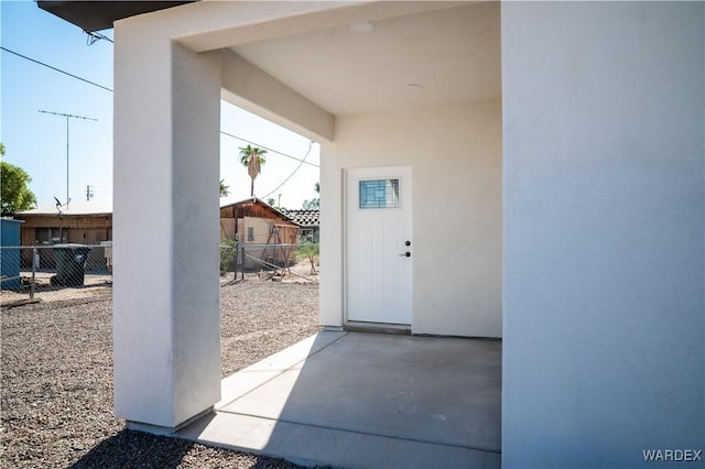 view of exterior entry featuring stucco siding, fence, and a patio