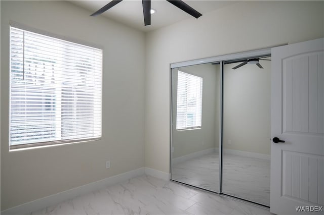 unfurnished bedroom featuring ceiling fan, marble finish floor, a closet, and baseboards