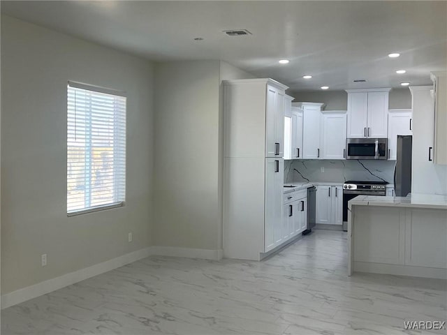 kitchen with appliances with stainless steel finishes, light countertops, marble finish floor, and white cabinetry