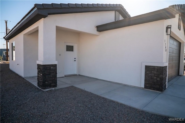 view of exterior entry with a garage, stone siding, and stucco siding