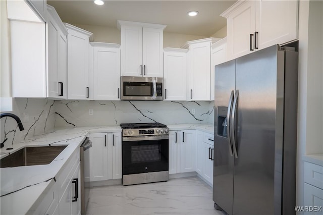 kitchen with light stone counters, stainless steel appliances, a sink, white cabinets, and marble finish floor