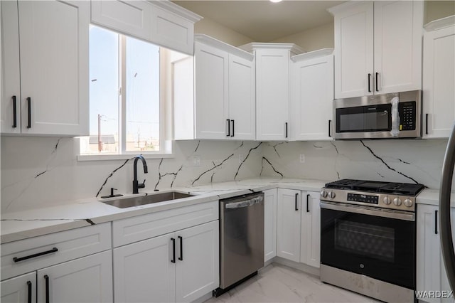 kitchen with stainless steel appliances, a sink, light stone countertops, and white cabinets