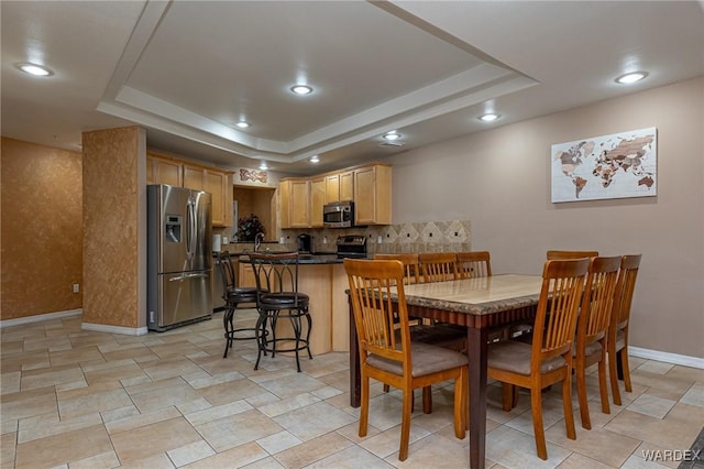 dining room with a tray ceiling, baseboards, and recessed lighting