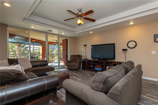 living room with a tray ceiling, recessed lighting, a ceiling fan, wood finished floors, and baseboards