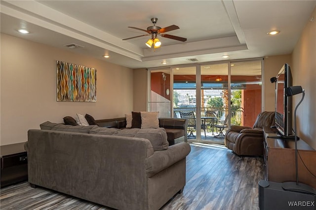 living room featuring dark wood-type flooring, visible vents, a ceiling fan, a wall of windows, and a raised ceiling