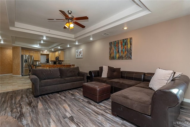 living room with baseboards, visible vents, ceiling fan, wood finished floors, and a tray ceiling