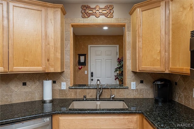 kitchen with dark stone counters, light brown cabinetry, stainless steel dishwasher, and a sink