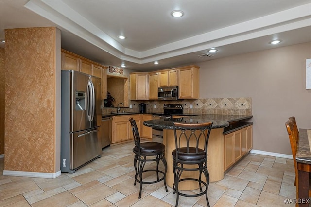 kitchen with tasteful backsplash, appliances with stainless steel finishes, dark stone counters, a peninsula, and a kitchen breakfast bar