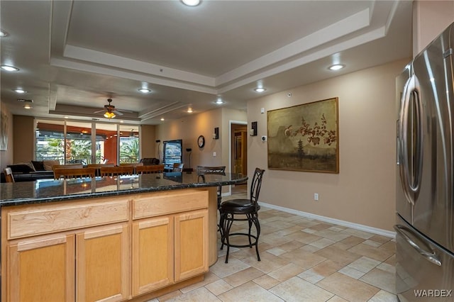 kitchen featuring open floor plan, freestanding refrigerator, dark stone counters, a raised ceiling, and a kitchen bar