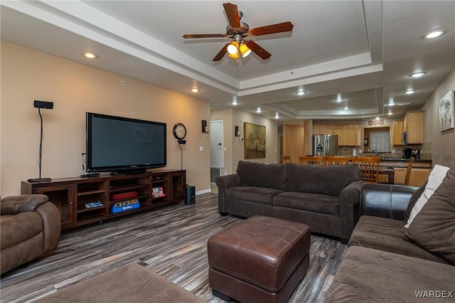 living room with a tray ceiling, dark wood finished floors, recessed lighting, a ceiling fan, and baseboards