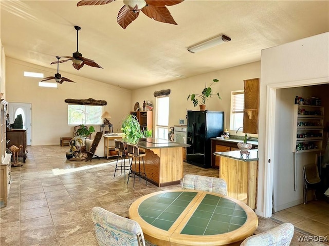 kitchen with lofted ceiling, a breakfast bar area, a center island, black fridge, and a sink