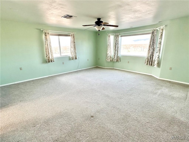 carpeted empty room with visible vents, plenty of natural light, baseboards, and ceiling fan