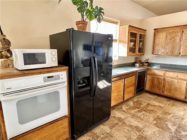 kitchen featuring black appliances, brown cabinetry, dark countertops, and glass insert cabinets