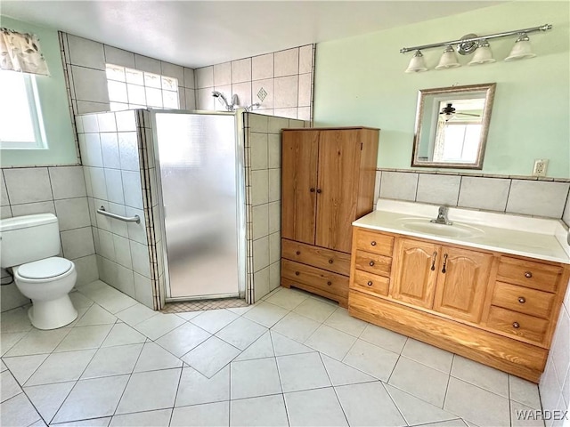 bathroom with tile patterned flooring, toilet, vanity, tile walls, and a stall shower