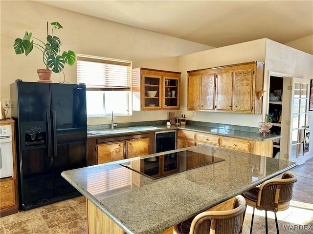 kitchen featuring stone countertops, a breakfast bar, brown cabinets, black appliances, and a sink