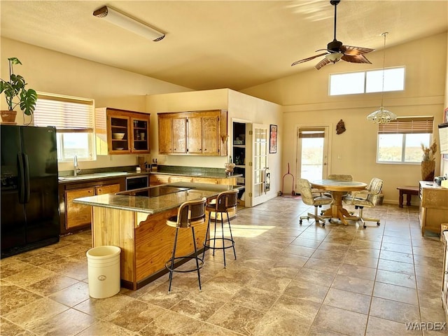 kitchen featuring brown cabinets, dark countertops, a sink, black appliances, and a kitchen bar