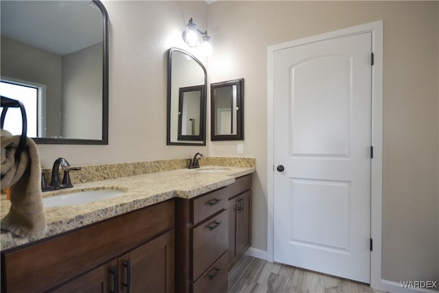 full bathroom with double vanity, wood finished floors, a sink, and baseboards