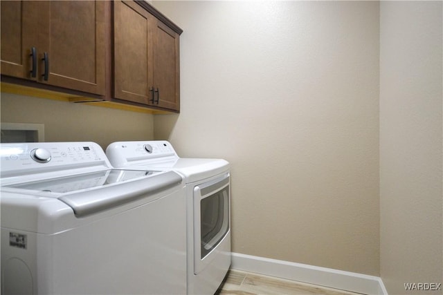 washroom with light wood-type flooring, cabinet space, baseboards, and washer and clothes dryer