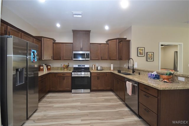 kitchen with visible vents, a peninsula, light stone countertops, stainless steel appliances, and a sink