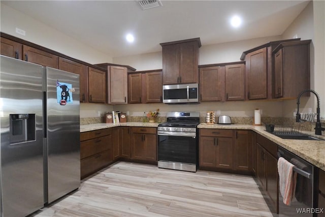 kitchen featuring visible vents, appliances with stainless steel finishes, a sink, dark brown cabinets, and light stone countertops