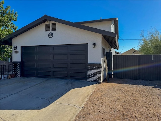 1189 Juanita Ln, Bullhead City, AZ 86442 - view of side of home with brick siding, concrete driveway, stucco siding, and a garage