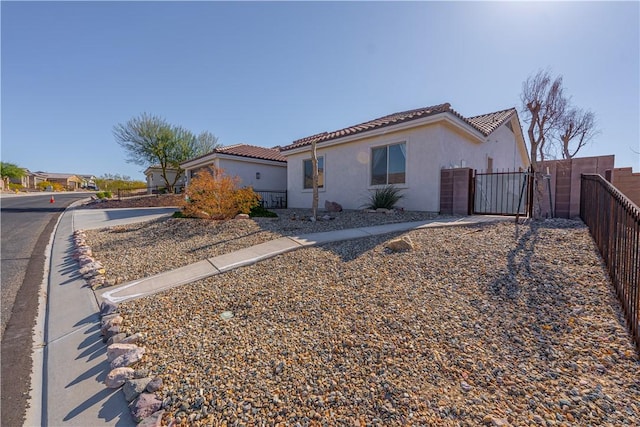 view of side of property with a gate, fence, a tile roof, and stucco siding