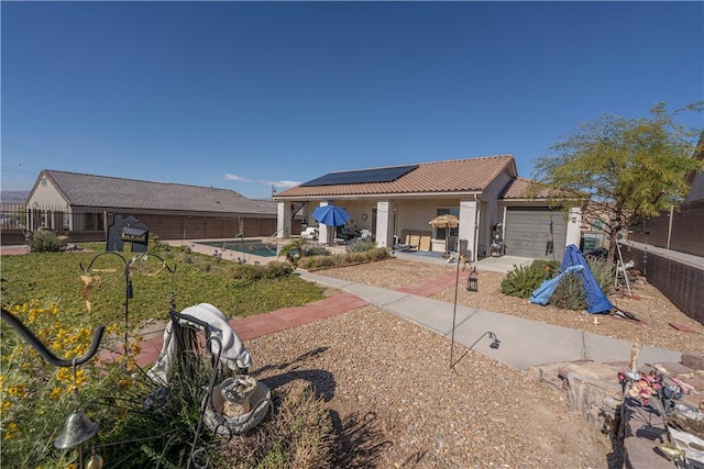 rear view of property featuring a tile roof, roof mounted solar panels, an attached garage, stucco siding, and a fenced backyard
