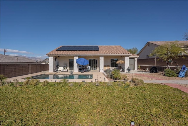 rear view of house with roof mounted solar panels, a tile roof, stucco siding, a patio, and a garage