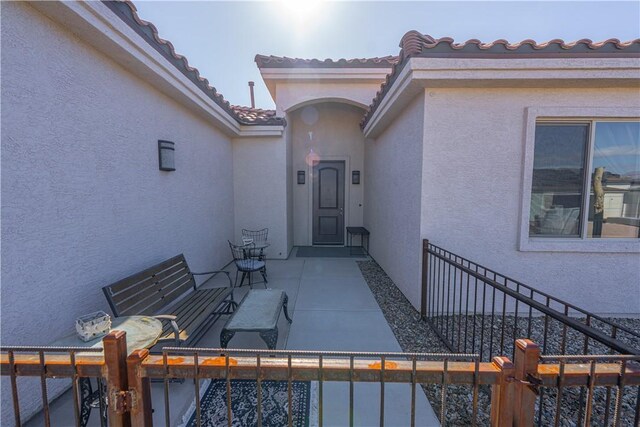 entrance to property with stucco siding, a tiled roof, and fence