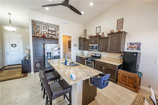 kitchen with appliances with stainless steel finishes, a sink, dark brown cabinets, a breakfast bar area, and ceiling fan