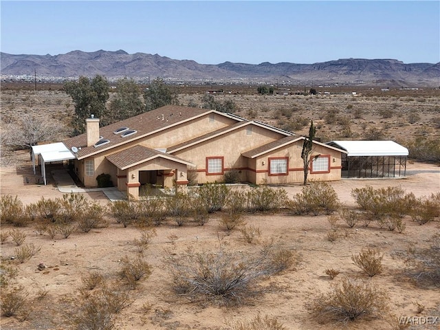 view of front of house with stucco siding, a mountain view, and a chimney