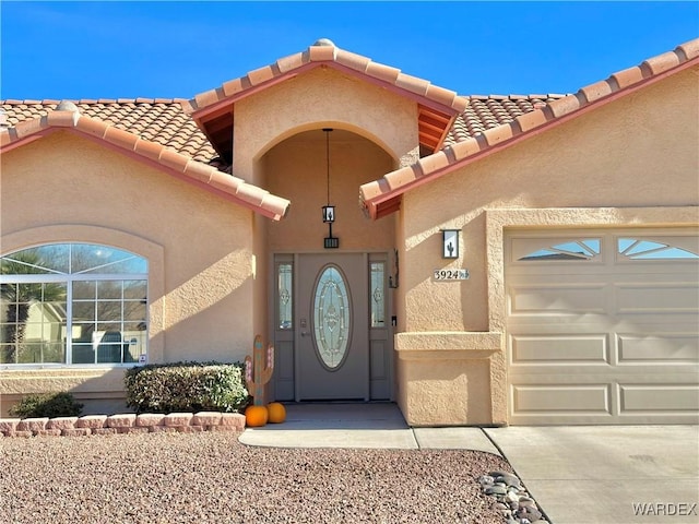 view of exterior entry with an attached garage, a tiled roof, and stucco siding