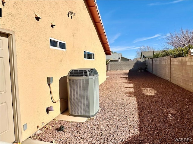 view of side of home with stucco siding, a fenced backyard, and central AC unit