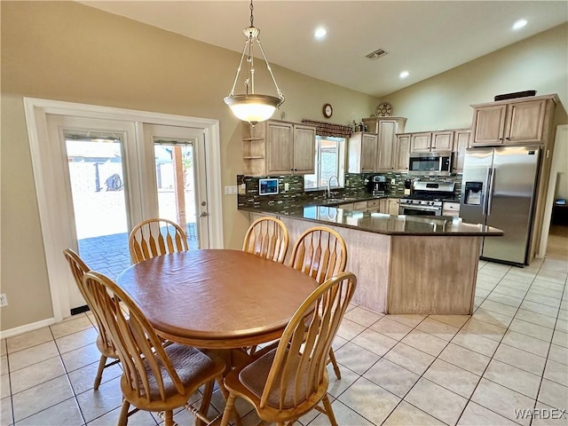 kitchen with stainless steel appliances, a peninsula, a sink, hanging light fixtures, and dark countertops