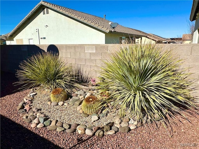 view of side of home featuring a tile roof, fence, and stucco siding