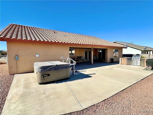 back of house with stucco siding, a hot tub, an outdoor kitchen, a patio area, and a tiled roof