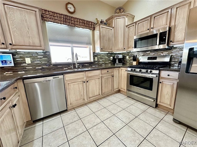 kitchen featuring appliances with stainless steel finishes, a sink, backsplash, and dark stone countertops