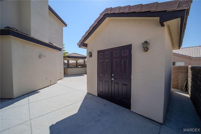 property entrance with fence, a patio, and stucco siding